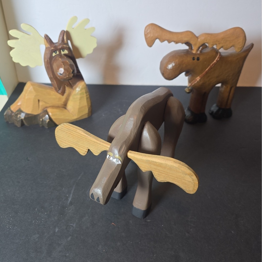 Lot of 3 rustic wooden moose figurines in assorted styles.